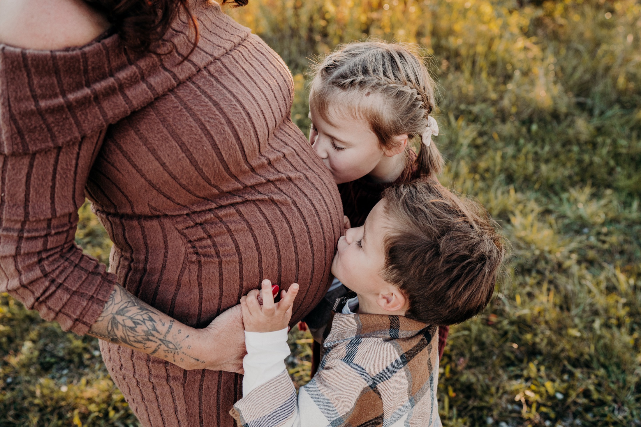 Geschwister geben dem Babybauch ihrer Mama einen Kuss